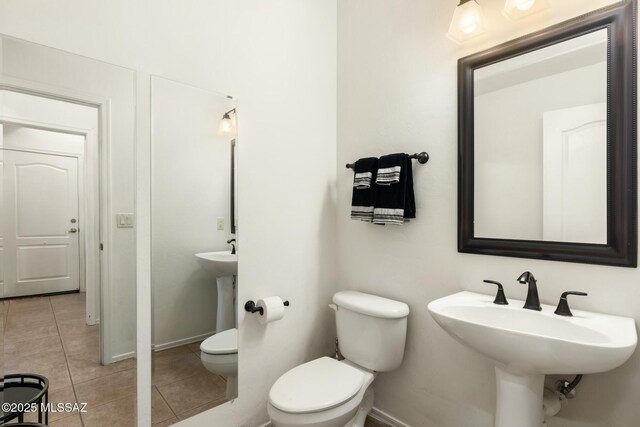 half bathroom with toilet, baseboards, a sink, and tile patterned floors