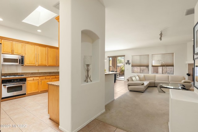 kitchen with light tile patterned floors, a skylight, visible vents, open floor plan, and stainless steel appliances