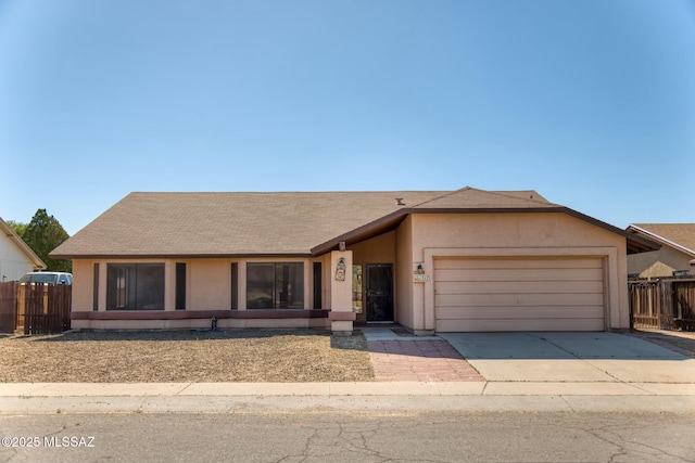 ranch-style home with a garage, a shingled roof, fence, concrete driveway, and stucco siding