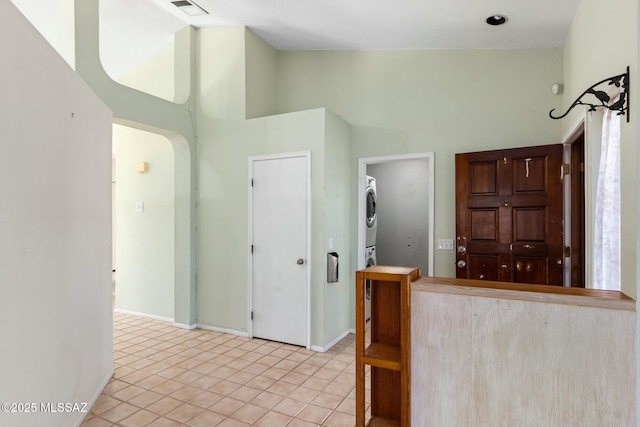 kitchen featuring high vaulted ceiling, light tile patterned flooring, stacked washer and dryer, visible vents, and baseboards