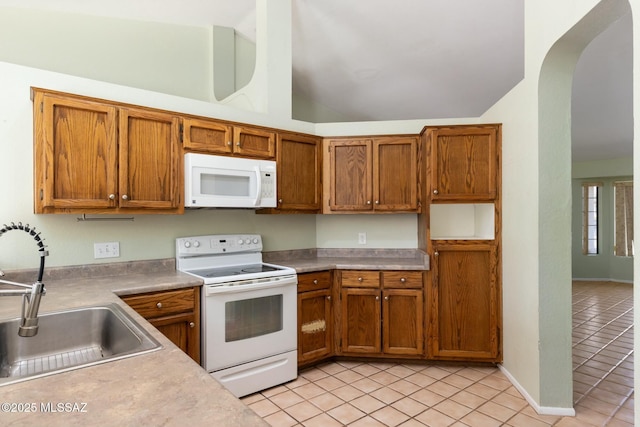 kitchen featuring lofted ceiling, white appliances, a sink, and brown cabinets