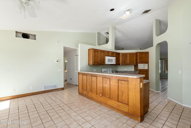 kitchen featuring arched walkways, brown cabinets, light countertops, white microwave, and light tile patterned flooring