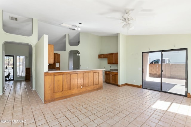 kitchen featuring light tile patterned floors, visible vents, arched walkways, lofted ceiling, and a peninsula