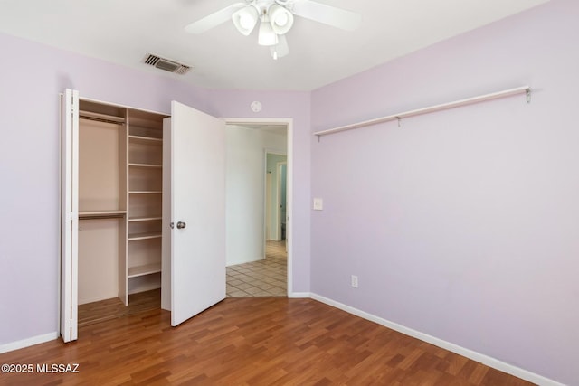 unfurnished bedroom with a closet, visible vents, a ceiling fan, wood finished floors, and baseboards