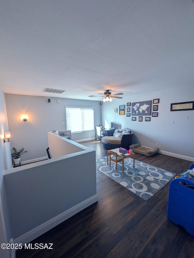 living area with ceiling fan, wood finished floors, visible vents, and baseboards