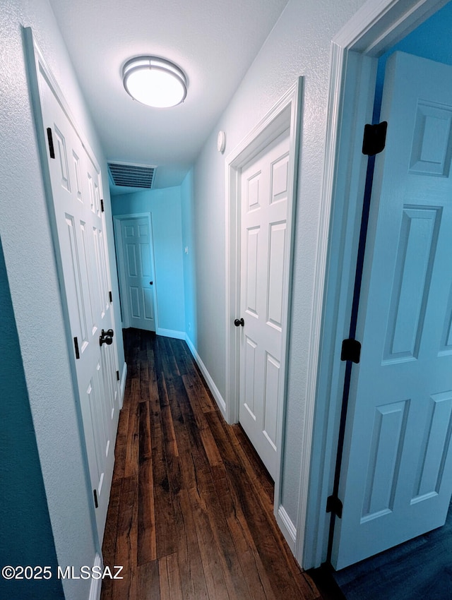 hallway featuring visible vents, dark wood finished floors, and baseboards