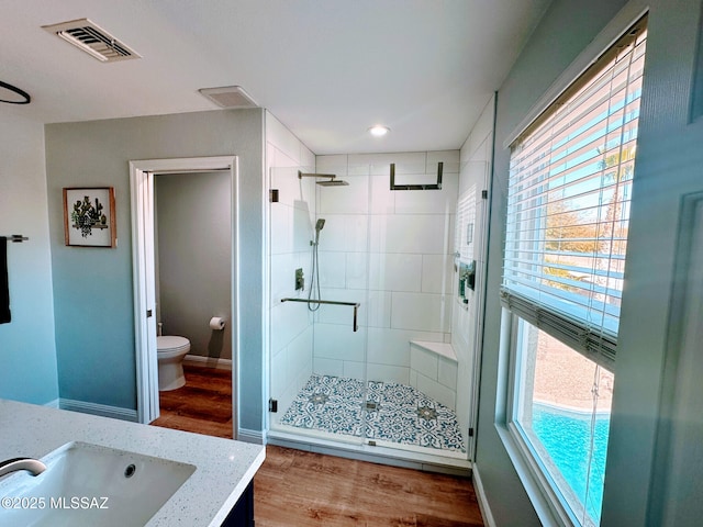 bathroom featuring visible vents, toilet, a shower stall, wood finished floors, and baseboards