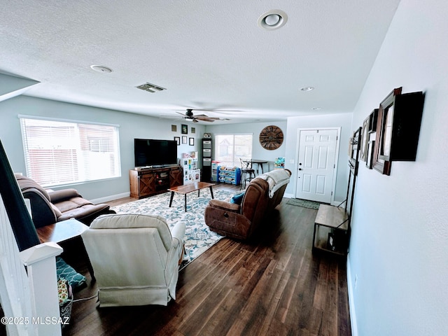 living room with baseboards, visible vents, a ceiling fan, dark wood finished floors, and a textured ceiling