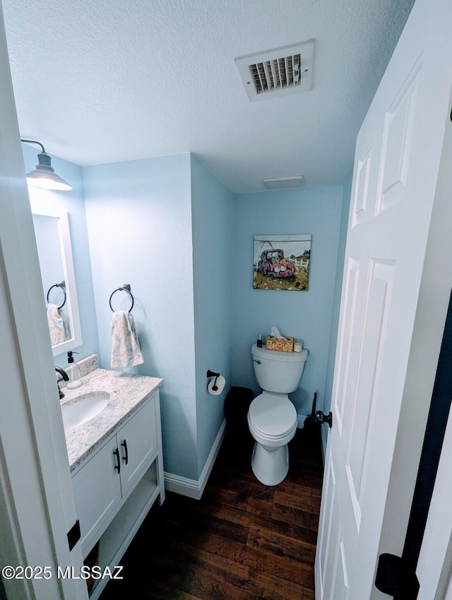 half bathroom featuring visible vents, toilet, vanity, a textured ceiling, and wood finished floors