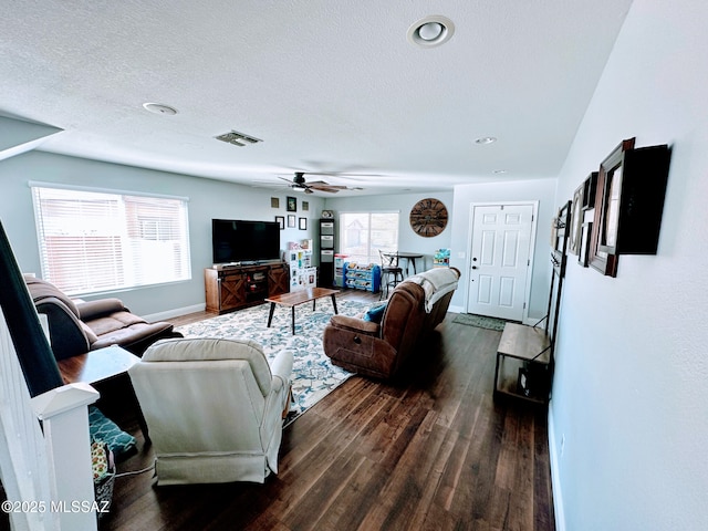 living room featuring baseboards, visible vents, a ceiling fan, dark wood-style flooring, and a textured ceiling