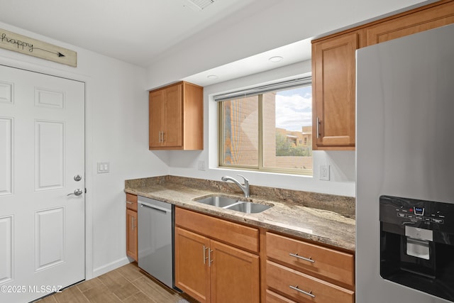 kitchen with brown cabinetry, light stone countertops, light wood finished floors, a sink, and stainless steel appliances