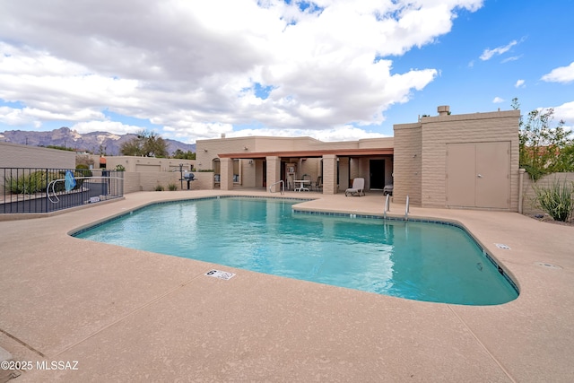 community pool with a mountain view, fence, and a patio area