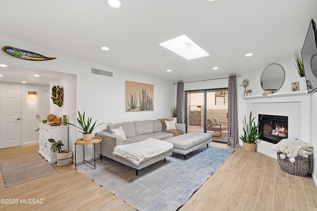 living room with visible vents, a skylight, recessed lighting, a glass covered fireplace, and light wood-type flooring