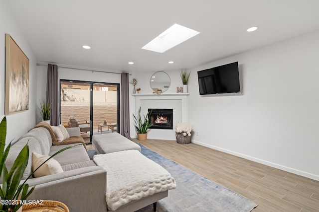 living area with a warm lit fireplace, wood finished floors, recessed lighting, a skylight, and baseboards