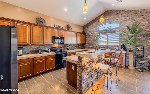 kitchen featuring light countertops, decorative backsplash, brown cabinetry, black appliances, and a kitchen breakfast bar