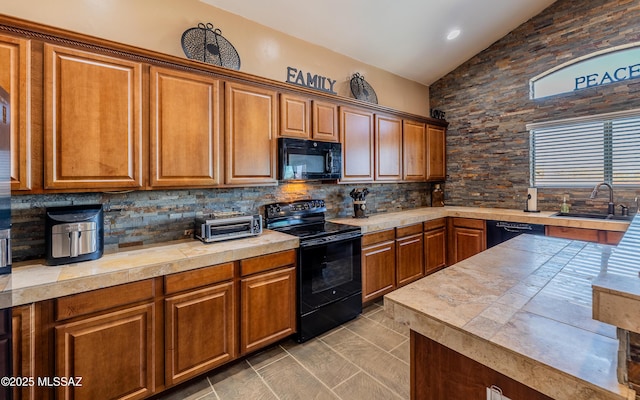 kitchen featuring lofted ceiling, a sink, black appliances, light countertops, and tasteful backsplash