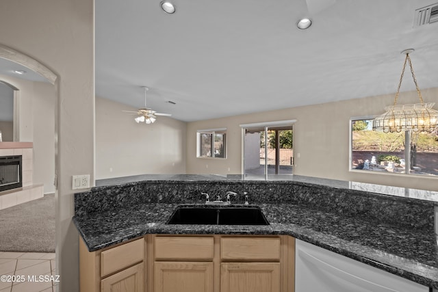 kitchen featuring white dishwasher, a tile fireplace, light colored carpet, a sink, and visible vents