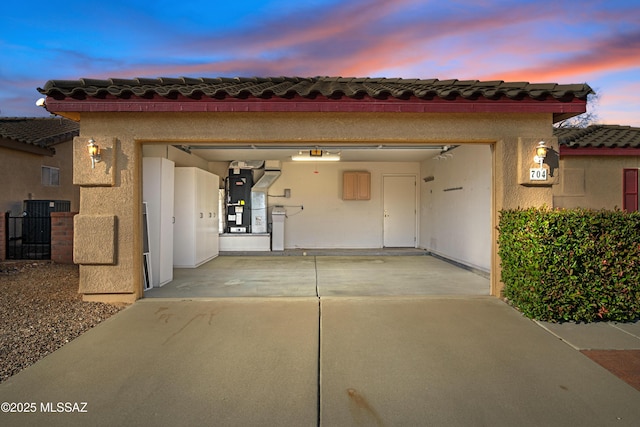 exterior space with a garage, a tile roof, concrete driveway, heating unit, and stucco siding