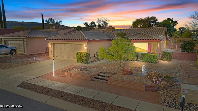 view of front of house with an attached garage, a tile roof, driveway, stucco siding, and a chimney