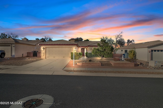 mediterranean / spanish-style home with a garage, driveway, a tiled roof, and stucco siding