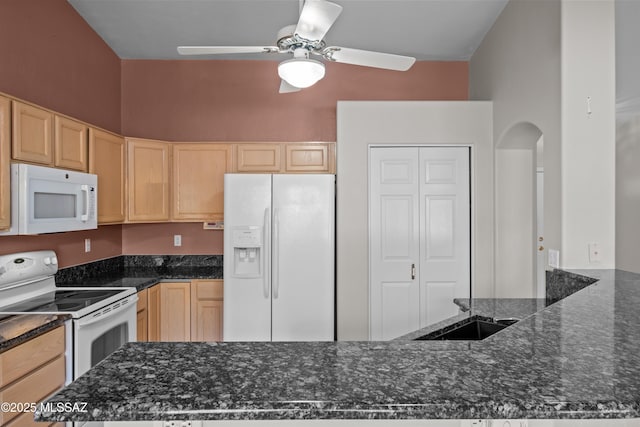 kitchen featuring dark stone counters, white appliances, a sink, and light brown cabinetry