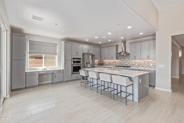 kitchen with wall chimney range hood, visible vents, stainless steel appliances, and gray cabinetry