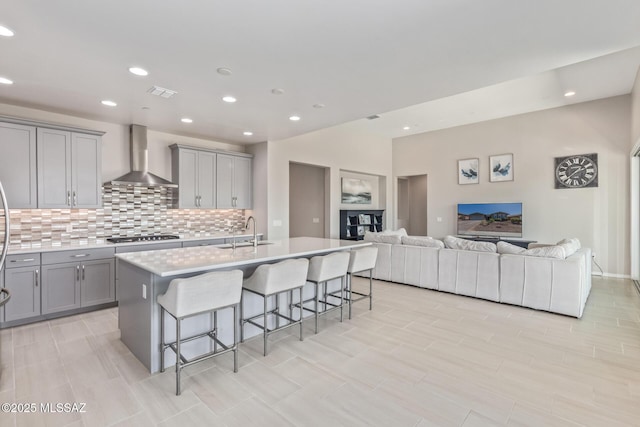 kitchen featuring a kitchen bar, gray cabinetry, a sink, open floor plan, and wall chimney exhaust hood