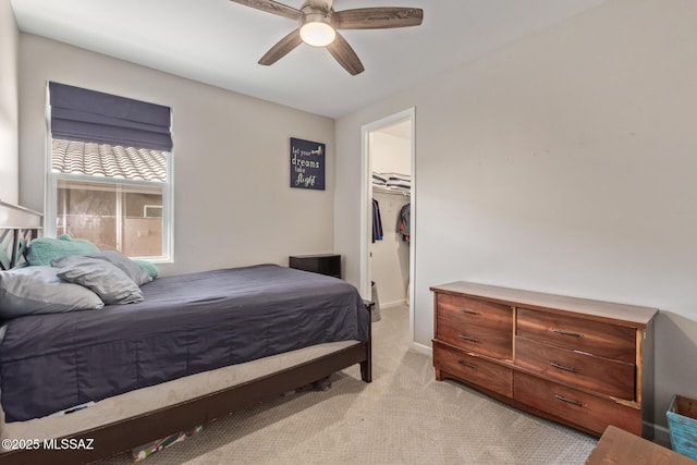 bedroom featuring a ceiling fan, baseboards, a closet, light carpet, and a walk in closet