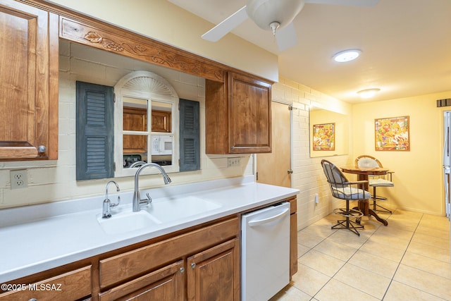 kitchen with light tile patterned floors, white dishwasher, a sink, light countertops, and brown cabinets