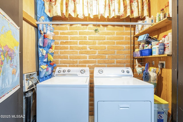 washroom featuring brick wall, laundry area, and washing machine and clothes dryer