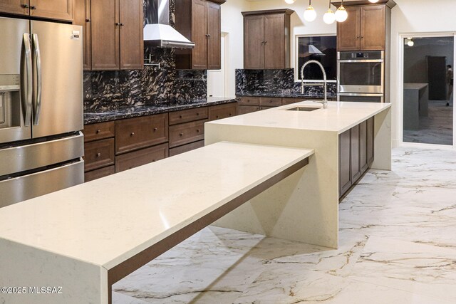 kitchen with tasteful backsplash, a sink, marble finish floor, wall chimney exhaust hood, and appliances with stainless steel finishes
