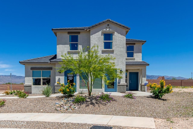 view of front of property with a tiled roof, fence, a mountain view, and stucco siding