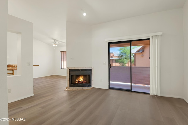 unfurnished living room featuring a ceiling fan, a wealth of natural light, a tiled fireplace, and wood finished floors