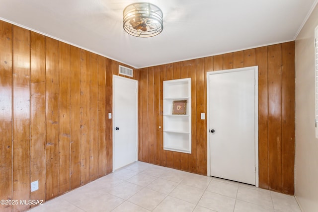 empty room with wood walls, tile patterned flooring, visible vents, and crown molding