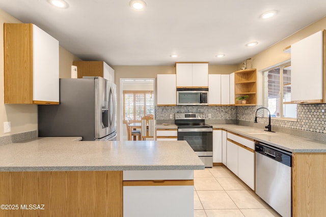 kitchen featuring a peninsula, white cabinetry, stainless steel appliances, and a sink