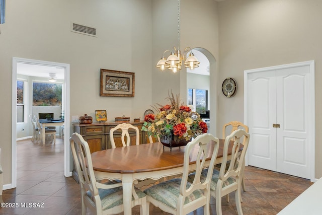 dining space with visible vents, dark tile patterned floors, a high ceiling, an inviting chandelier, and arched walkways