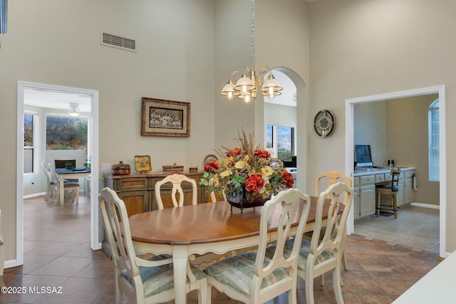 tiled dining area with visible vents, a towering ceiling, arched walkways, baseboards, and a chandelier