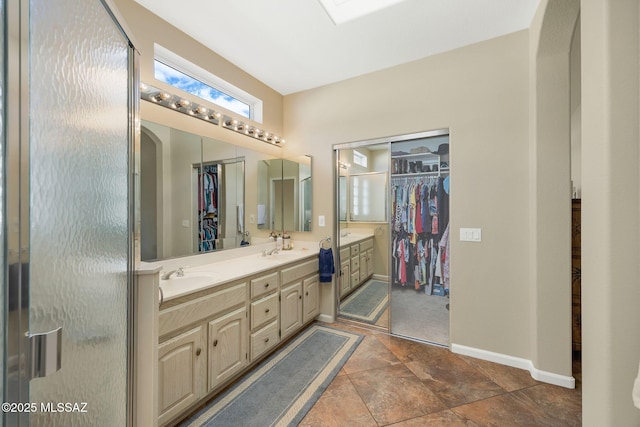 bathroom with double vanity, a walk in closet, baseboards, and a sink