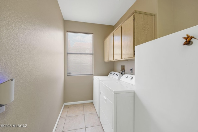 laundry area featuring washing machine and dryer, light tile patterned floors, cabinet space, and baseboards