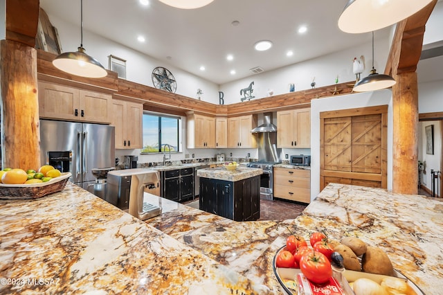 kitchen featuring a kitchen island, a towering ceiling, appliances with stainless steel finishes, light brown cabinetry, and wall chimney exhaust hood