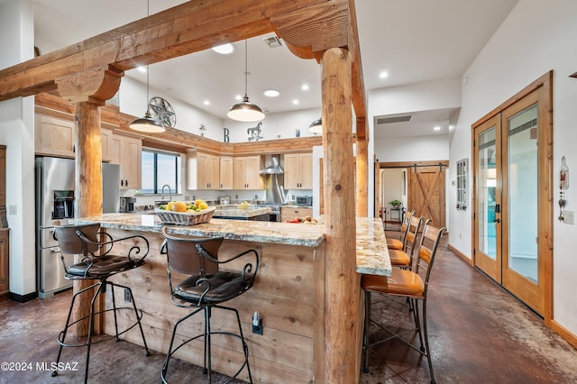 kitchen with a barn door, finished concrete flooring, light stone countertops, wall chimney exhaust hood, and ornate columns