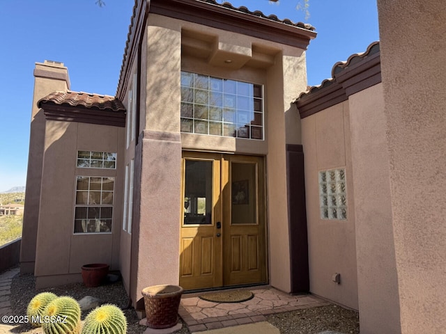 entrance to property with a chimney, a tile roof, and stucco siding