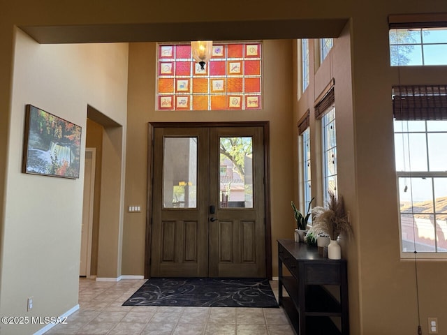 foyer with french doors, baseboards, a high ceiling, and light tile patterned floors