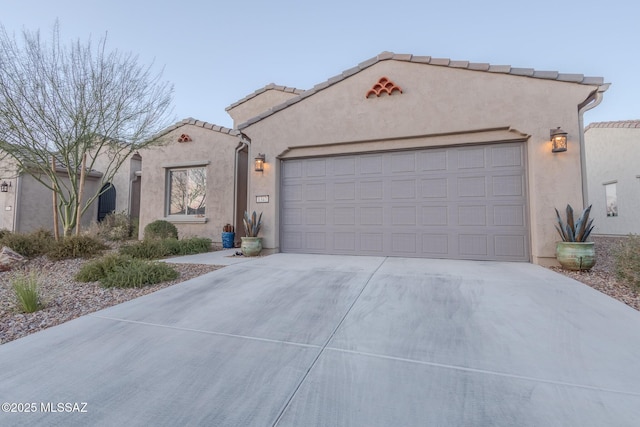 mediterranean / spanish-style home with an attached garage, driveway, a tiled roof, and stucco siding