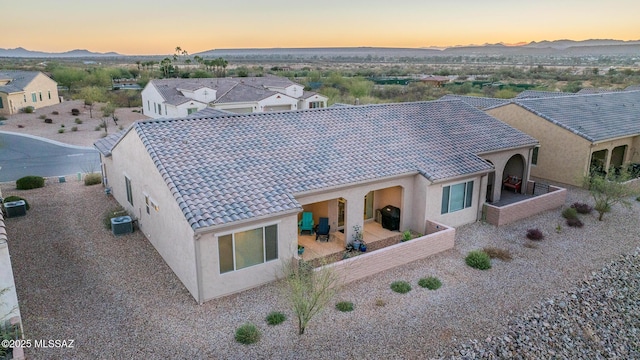 back of house at dusk with stucco siding, a tile roof, a mountain view, and central air condition unit