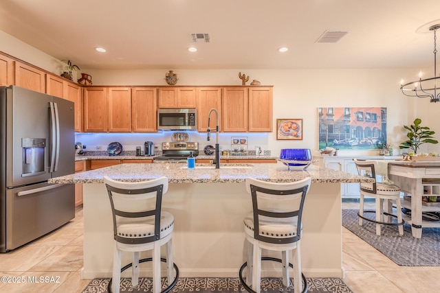 kitchen featuring an island with sink, visible vents, appliances with stainless steel finishes, and light stone counters