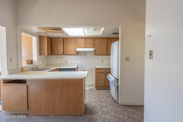 kitchen with freestanding refrigerator, a peninsula, light countertops, under cabinet range hood, and a sink