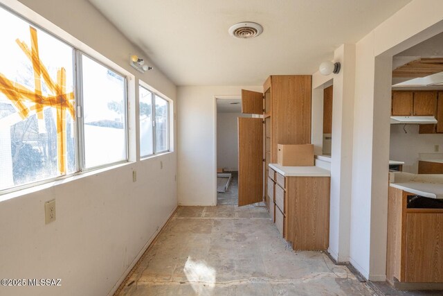 kitchen with light countertops, brown cabinets, visible vents, and under cabinet range hood