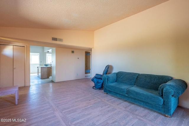 living room with lofted ceiling, a textured ceiling, visible vents, and wood finished floors