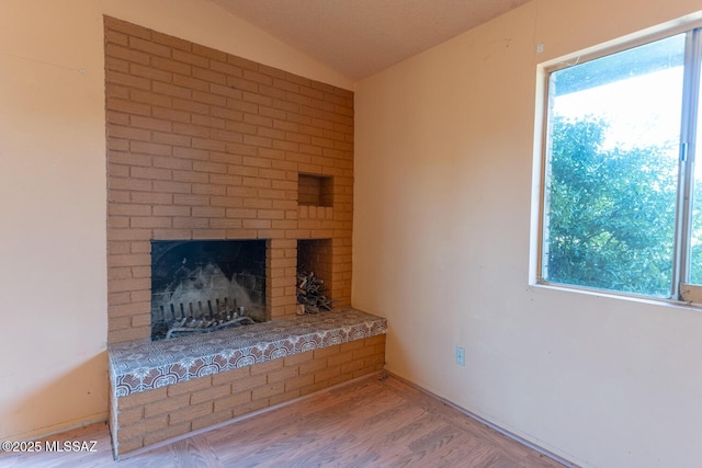 unfurnished living room with a brick fireplace, vaulted ceiling, and wood finished floors